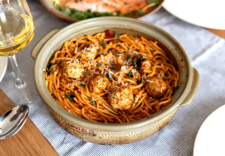 Spaghetti aux boulettes de viande dans un plat en céramique, parsemé de parmesan et d'herbes. Une recette facile et gourmande parfaite pour un repas convivial.