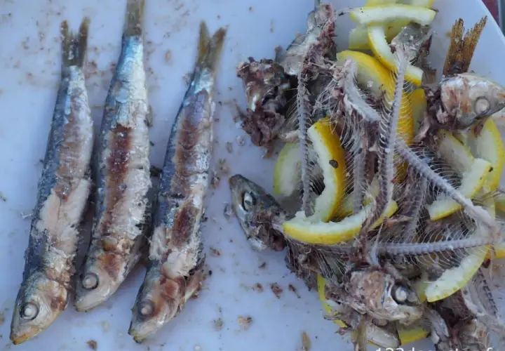Trois sardines grillées entières à gauche, et à droite, des arêtes de poisson avec des rondelles de citron.