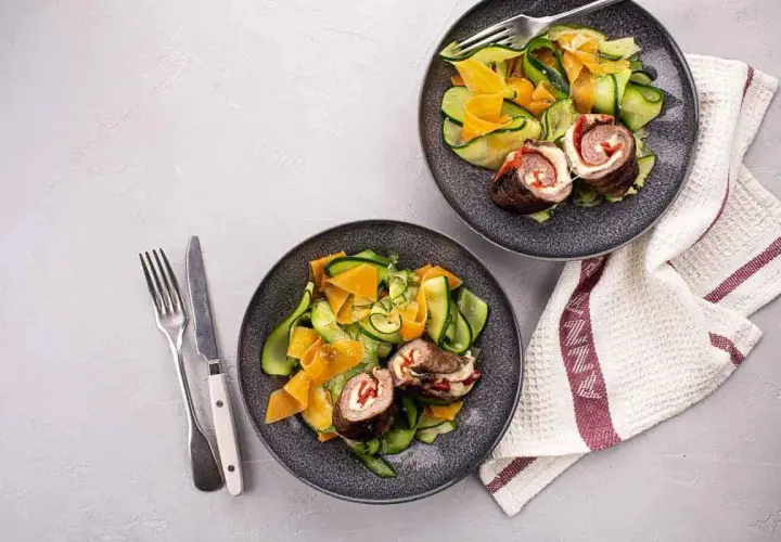 Deux assiettes de involtini, roulés de viande farcis, servis avec une salade de courgettes et carottes en rubans.