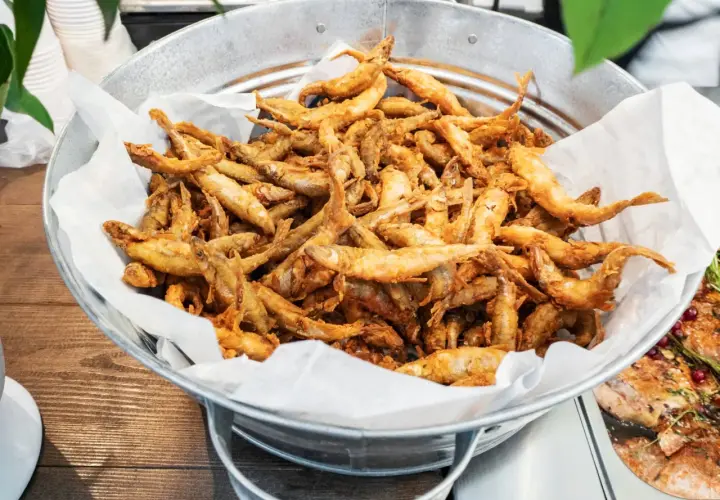 Un seau rempli d'éperlans frits dorés, prêts à être dégustés. Ces petits poissons croustillants sont un délice.