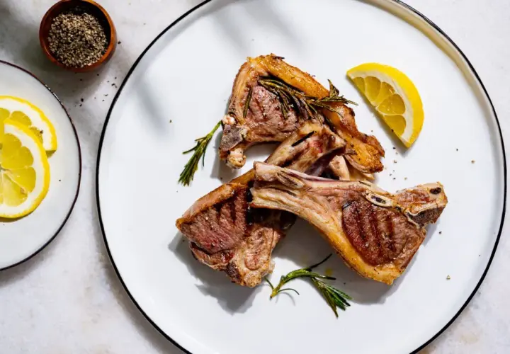 Trois côtelettes d'agneau grillées, garnies de romarin et de citron, prêtes pour le temps de cuisson idéal.