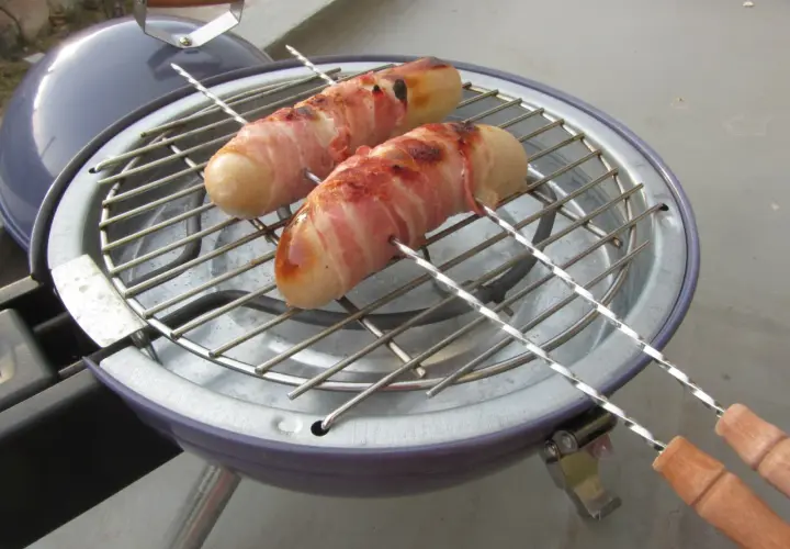 Deux boudins blancs enroulés de lard grillent sur un barbecue. Un délice pour un barbecue estival.
