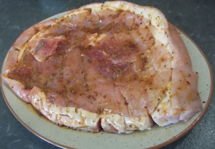 Rouelle de porc prête pour la plancha, généreusement recouverte d'une marinade savoureuse aux herbes et épices.