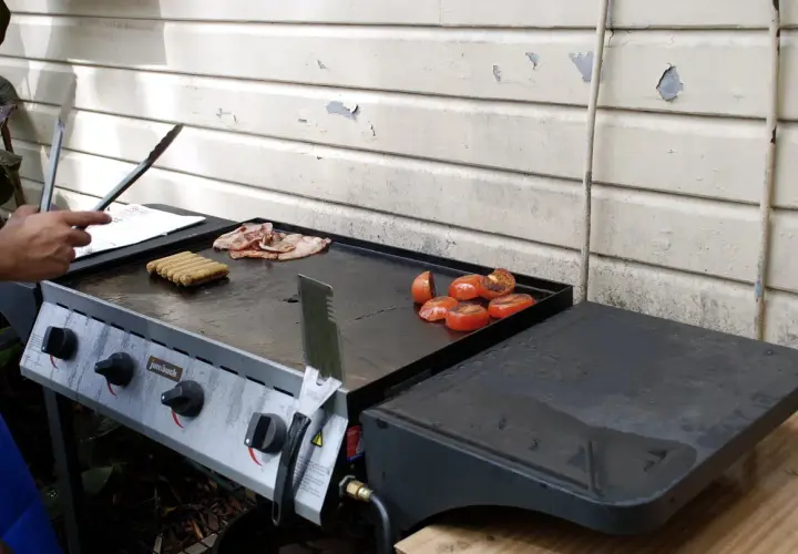 Un barbecue avec une bouteille de gaz prépare un petit-déjeuner savoureux : saucisses, bacon et tomates grillées.