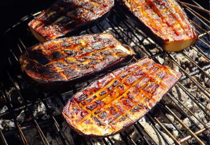 Aubergines coupées en deux, grillées au barbecue, avec des marques de cuisson caramélisées et une chair tendre.