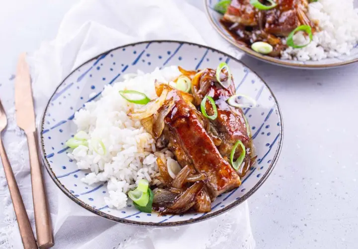Délicieux accompagnement travers de porc laqué, servi avec du riz blanc et garni d'oignons caramélisés et de ciboule.