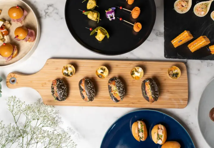 Assortiment de bouchées variées, parfaites pour un manger froid. Mini-burgers, tartes salées et sandwichs au saumon sur planche en bois.