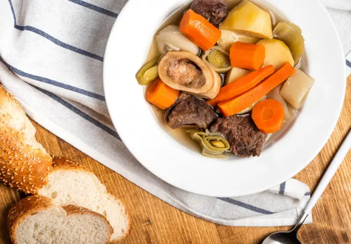 Un réconfortant pot-au-feu d'hiver avec du bœuf, des carottes, des poireaux et une os à moelle, servi avec du pain croustillant.