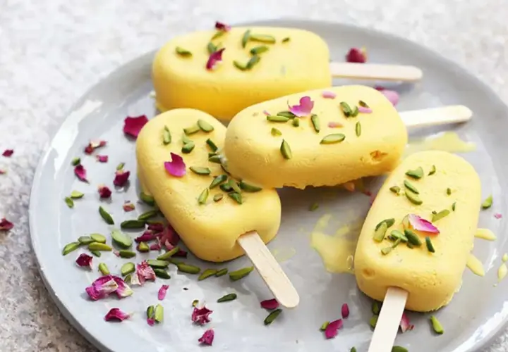 Quatre glaces jaunes, garnies de pistaches et de pétales de rose, sur une assiette. Un délicieux dessert iranien.