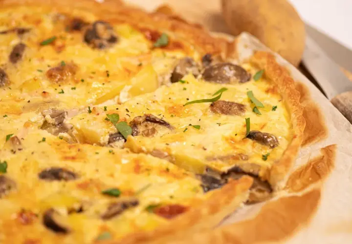 Une délicieuse quiche poulet pomme de terre, garnie de champignons et d'herbes fraîches, prête à être dégustée.