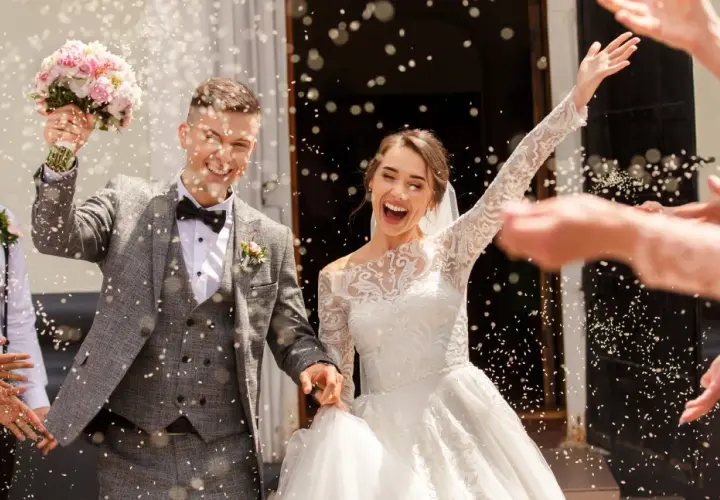 Jeune mariée et marié joyeux sortant de l'église sous une pluie de riz. Idées de mariage pour 20 personnes : une sortie mémorable !