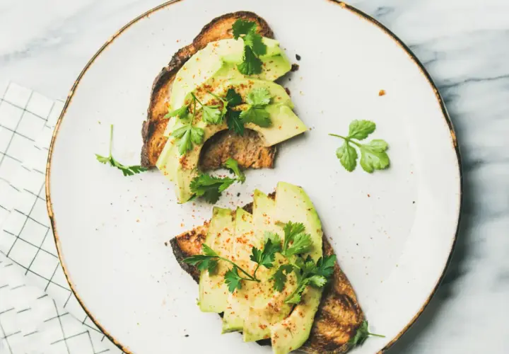 Deux toasts de pain grillé garnis de tranches d'avocat frais, parsemés d'épices et de persil. Une recette avocat simple et savoureuse.