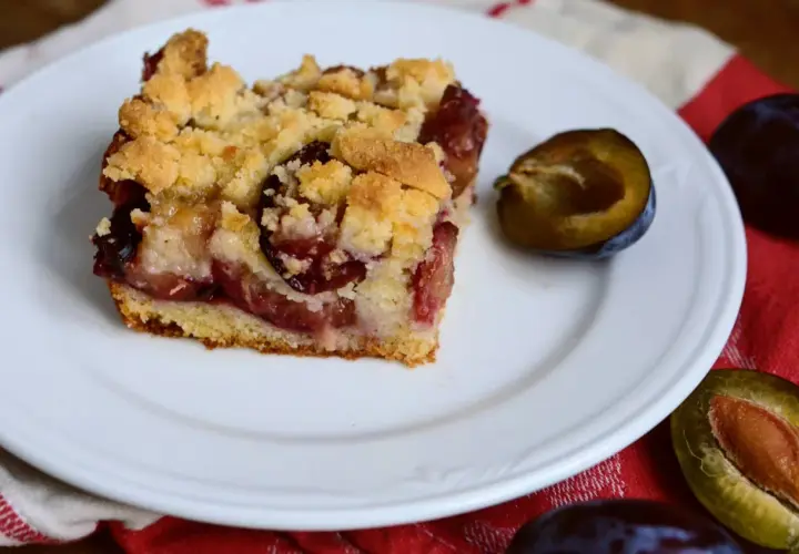 Tranche de gâteau aux prunes à la poêle, garnie de crumble doré et de fruits juteux. Une demi-prune à côté.