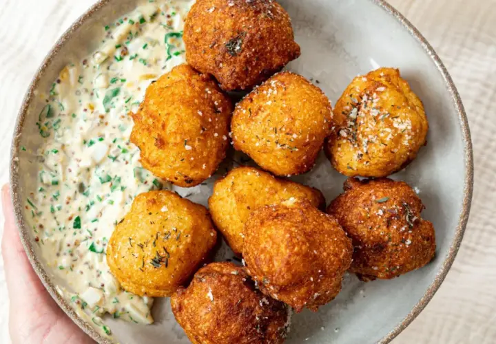 Un bol de pommes dauphines croustillantes, dorées et saupoudrées d'herbes, accompagnées d'une sauce crémeuse aux herbes et aux œufs.