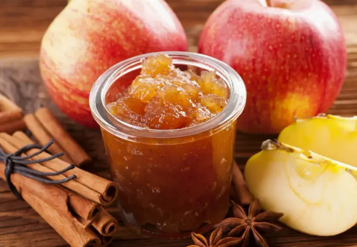 Un pot de confiture de pommes originales, avec des bâtons de cannelle, des étoiles de badiane et des pommes fraîches.