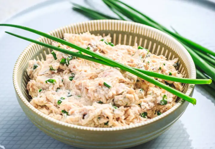 Un bol de rillettes de thon à la crème fraîche, garni de ciboule fraîche. Un délice crémeux et savoureux.