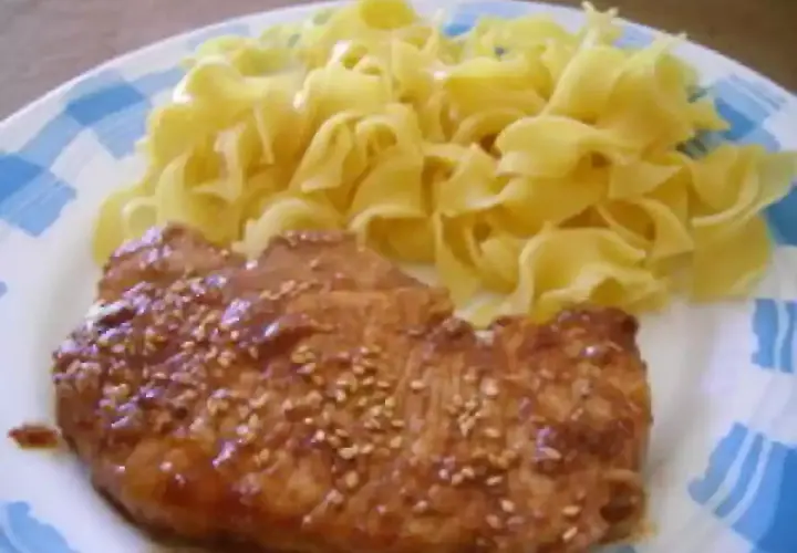 Une côte de porc savoureuse, nappée d'une sauce soja brillante et parsemée de graines de sésame, accompagnée de pâtes fraîches.