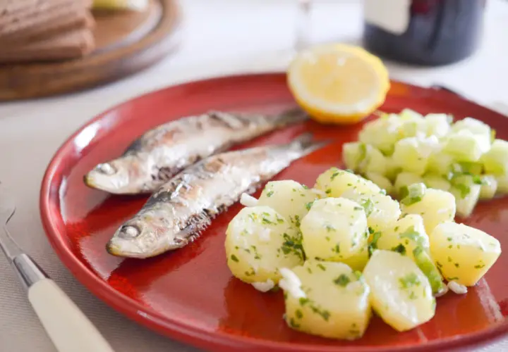 Deux sardines grillées sur une assiette rouge avec une salade de pommes de terre et de concombre. Quel accompagnement avec des sardines grillées !