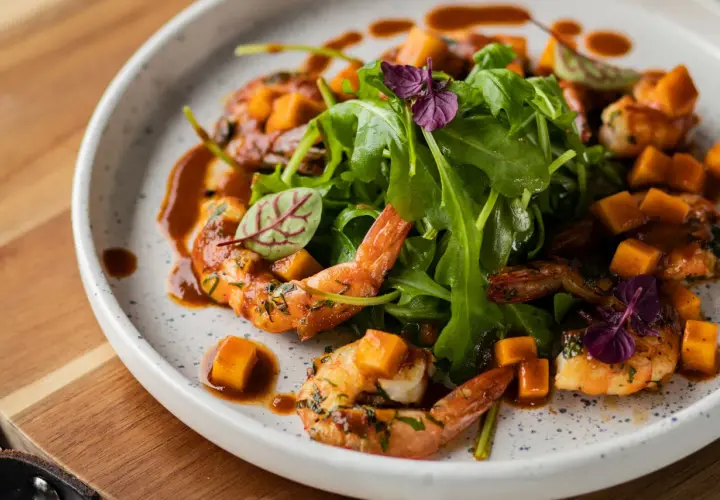 Assiette de crevettes flambées, cubes de mangue et roquette, arrosée d'une sauce caramélisée.