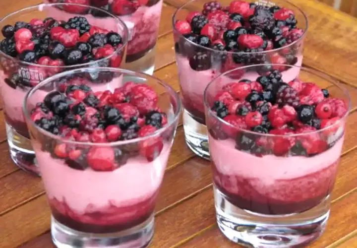 Plusieurs verrines de **dessert léger aux fruits rouges surgelés**, garnies de baies fraîches et d'une mousse rose.
