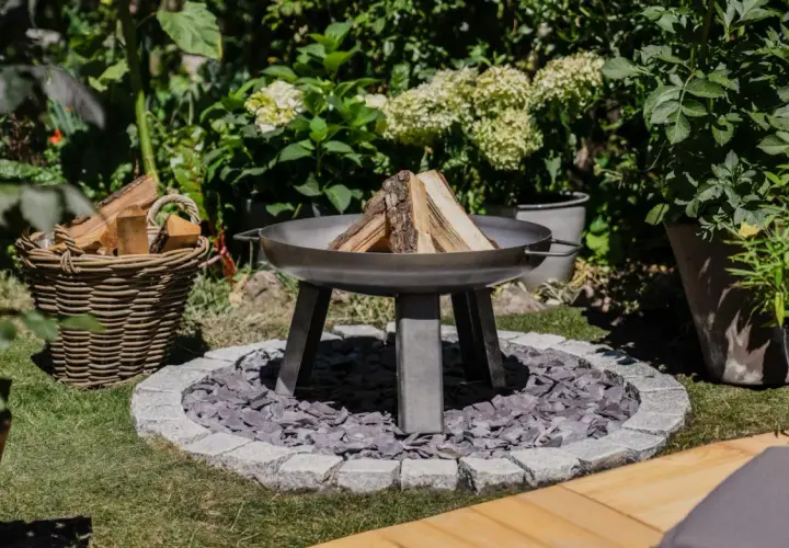 Un brasero en forme de chaudron, prêt à être allumé, avec du bois à côté. Un coin de jardin accueillant pour des soirées conviviales.