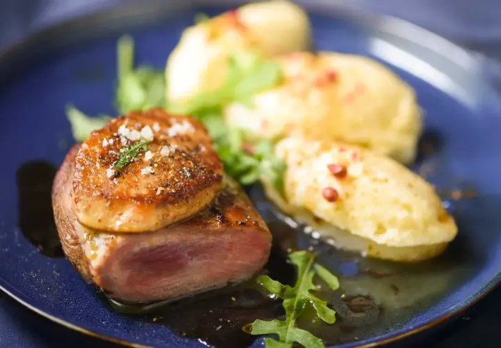 Tournedos de canard cuisson parfaite, garni de foie gras poêlé, servi avec une purée de pommes de terre et des roquettes.