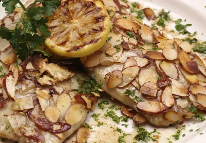 Deux filets de poisson recouverts d'amandes effilées grillées, garni de persil frais et d'une tranche de citron grillée. Un délice de truite aux amandes.