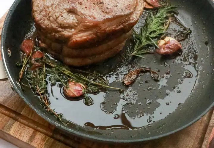 Rouelle de porc au barbecue, dorée et juteuse, mijotant dans une poêle avec de l'ail et des herbes aromatiques.