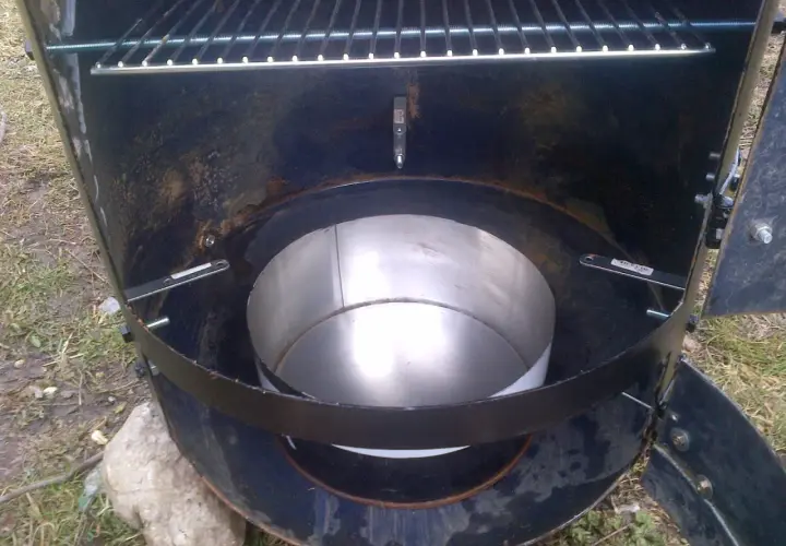 Intérieur d'un fumoir fait maison avec un bidon. Une grille est visible en haut, et un récipient métallique au centre.