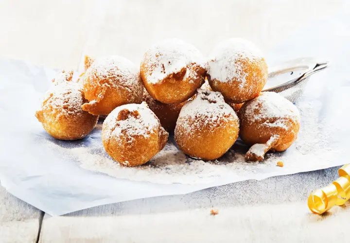 Des beignets dorés saupoudrés de sucre glace, ressemblant à des crottes d'âne, sur du papier bleu.