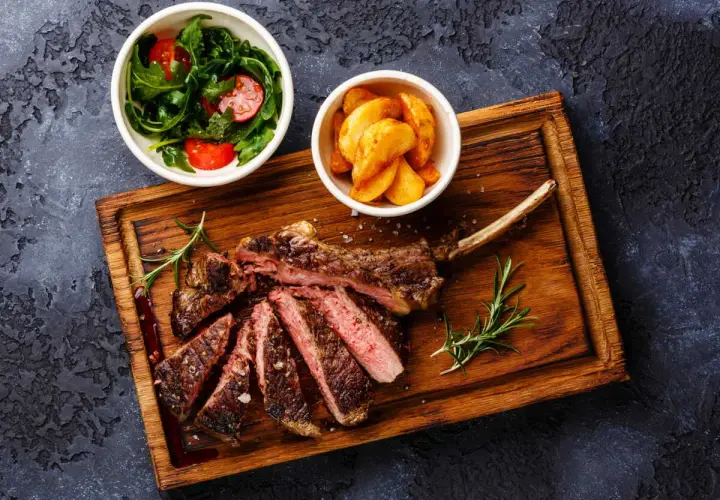 Un succulent accompagnement de côte de bœuf, servi avec une salade fraîche et des pommes de terre rôties sur une planche en bois.