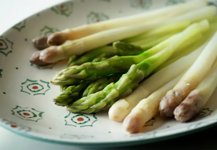 Asperges vertes et blanches sur une assiette décorée, prêtes pour la cuisson.
