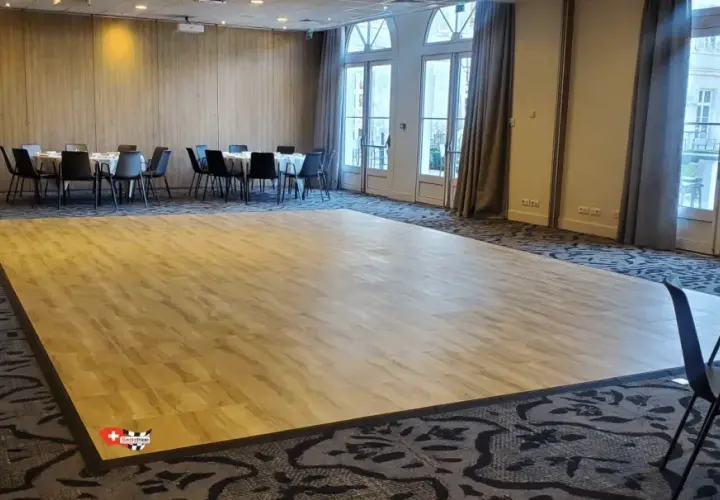 Une piste de danse en bois clair, idéale pour savoir comment faire une piste de danse pas cher. Des tables rondes et des chaises noires sont disposées autour.