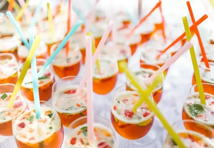 Des verres remplis de cocktails orange vif, garni de fruits et de menthe, avec des pailles colorées. Un parfait cocktail de bienvenue mariage.