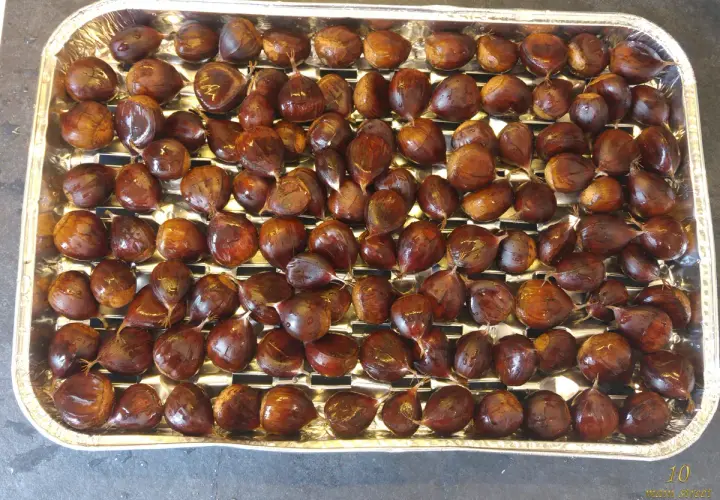 Plateau rempli de châtaignes prêtes à être grillées au barbecue. Elles sont brillantes et bien rangées.