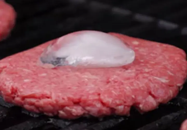 Un steak haché au barbecue, avec un glaçon posé dessus pour une cuisson parfaite.