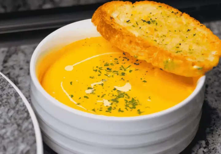 Soupe orange onctueuse, garnie d'herbes et d'un filet de crème, avec une tranche de pain à l'ail. Idéal pour savoir comment épaissir une soupe.