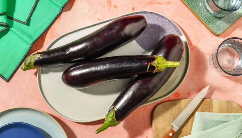 Trois aubergines allongées sur une assiette, prêtes pour des recettes d'été. Ces légumes de juin promettent de délicieux plats.