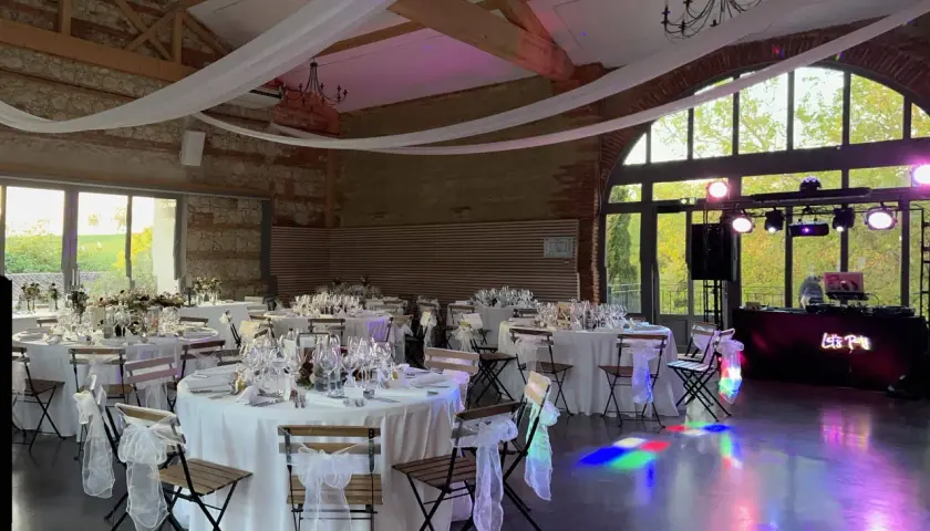 Salle de réception décorée pour un mariage de 80 personnes, tables dressées, lumières d'ambiance et DJ prêt à animer la soirée.