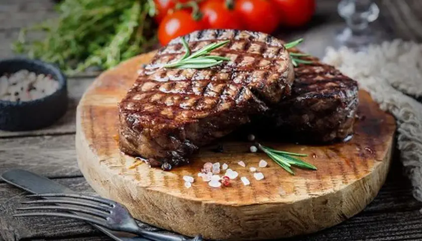 Deux steaks grillés sur une planche en bois, parsemés de gros sel rose. Une question se pose : quand saler la viande au barbecue pour un résultat parfait ?