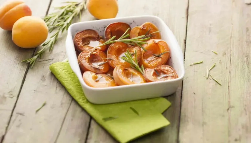 Abricots rôtis au four, tendres et caramélisés, garnis de romarin frais. Un délice simple et parfumé.