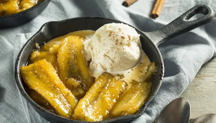 Bananes flambées au barbecue, servies chaudes dans une poêle en fonte avec une boule de glace à la vanille saupoudrée de cannelle.