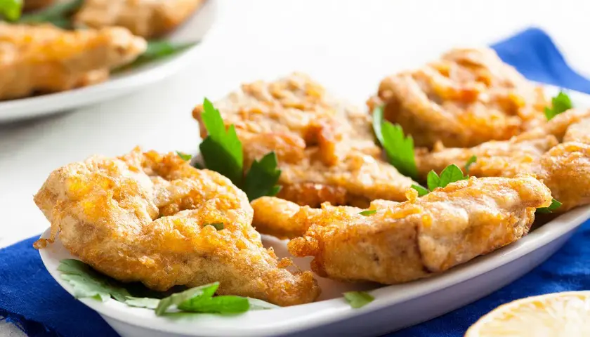 Délicieux artichaut frit, croustillant et doré, servi sur une assiette blanche avec des herbes fraîches et un quartier de citron.
