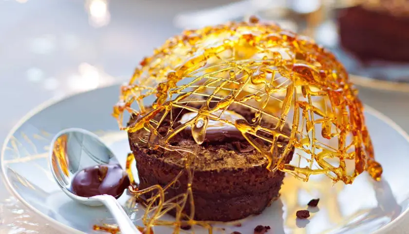 Gâteau au chocolat surmonté d'une décoration caramel facile et aérienne, avec une cuillère de sauce au chocolat.