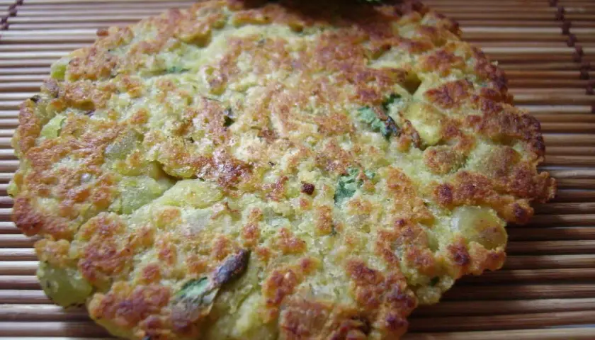 Une galette de pois cassés dorée et croustillante, garnie de persil frais, repose sur un tapis de bambou.