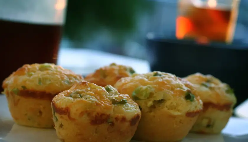 Cinq muffins salés dorés, garnis de fromage et d'herbes, sur une assiette blanche.