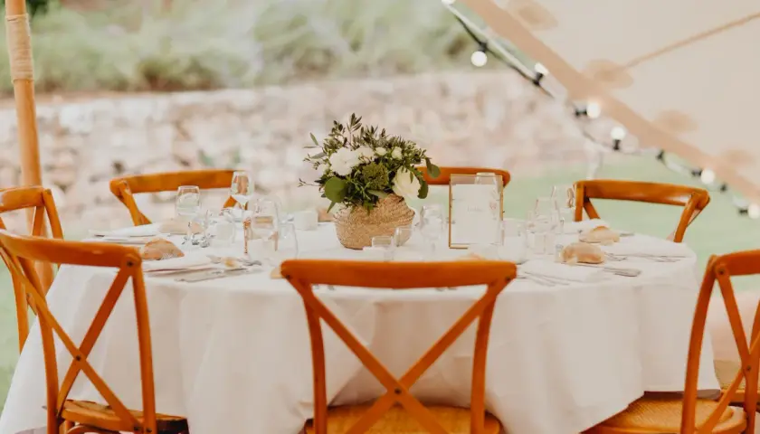 Table dressée pour un repas traditionnel mariage français, avec des chaises en bois, des fleurs et des petits pains.