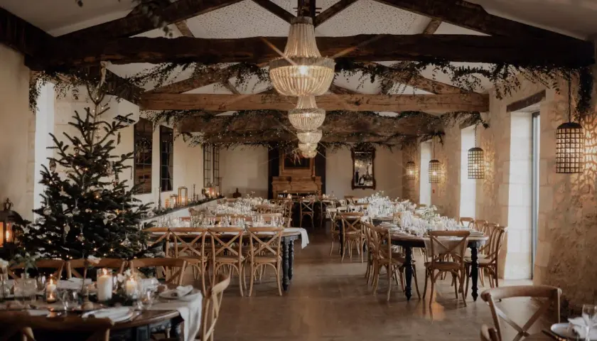 Une salle de réception décorée pour un mariage en hiver, avec un sapin illuminé, des guirlandes lumineuses et des tables dressées.