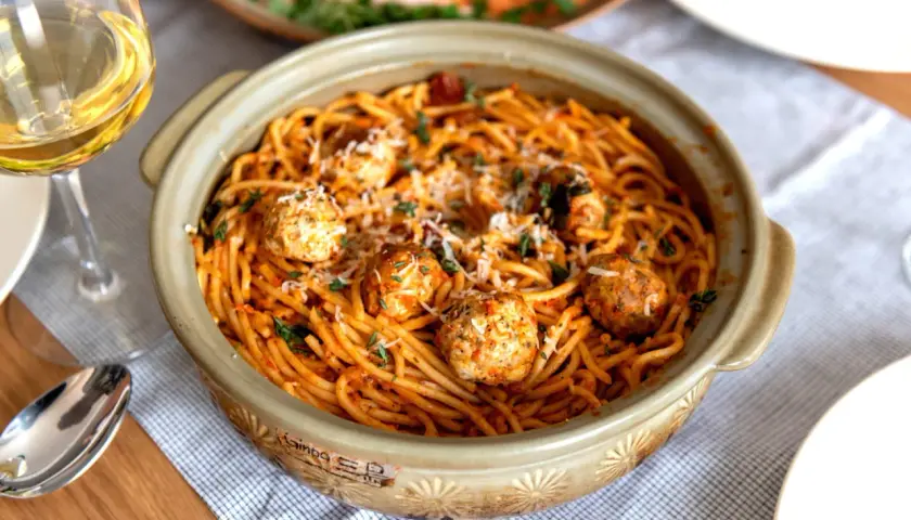 Spaghetti aux boulettes de viande dans un plat en céramique, parsemé de parmesan et d'herbes. Une recette facile et gourmande parfaite pour un repas convivial.