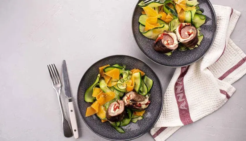 Deux assiettes de involtini, roulés de viande farcis, servis avec une salade de courgettes et carottes en rubans.